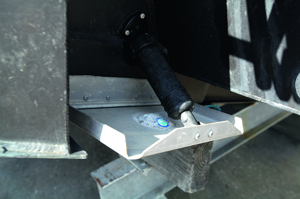 Hydraulic trim tab mounted on boat transom showing metal tab plate and ram for hull attitude adjustment.