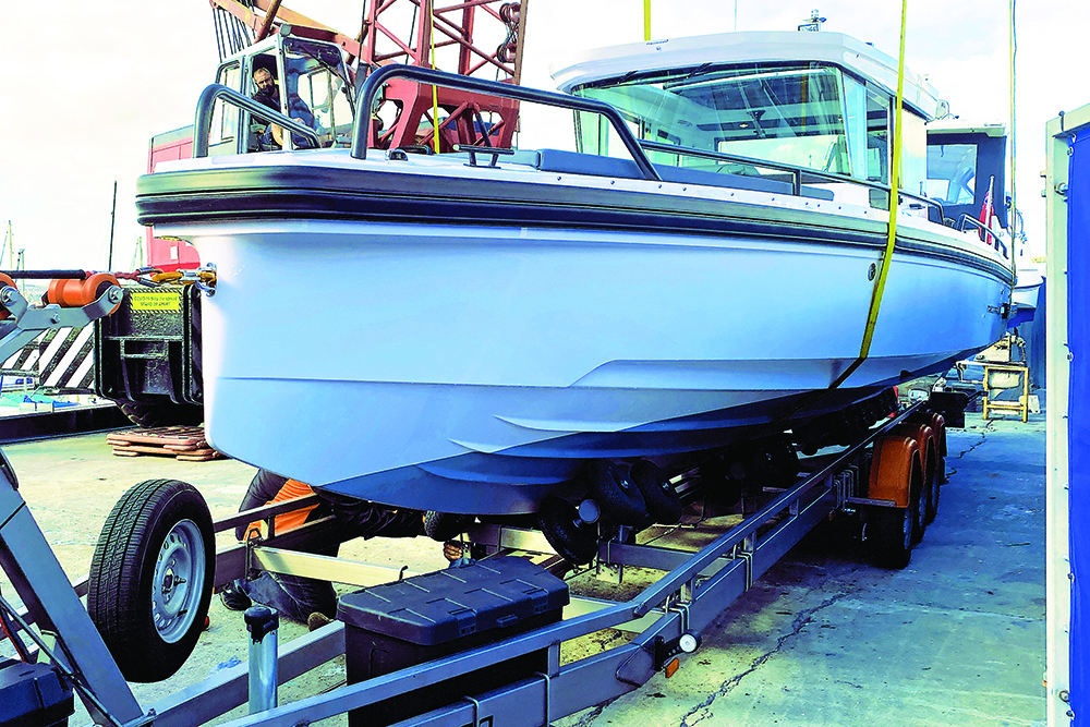 Axopar 28 Cabin secured on Vanclaes trailer in boatyard, showing hull support system and triple-axle setup for transport.