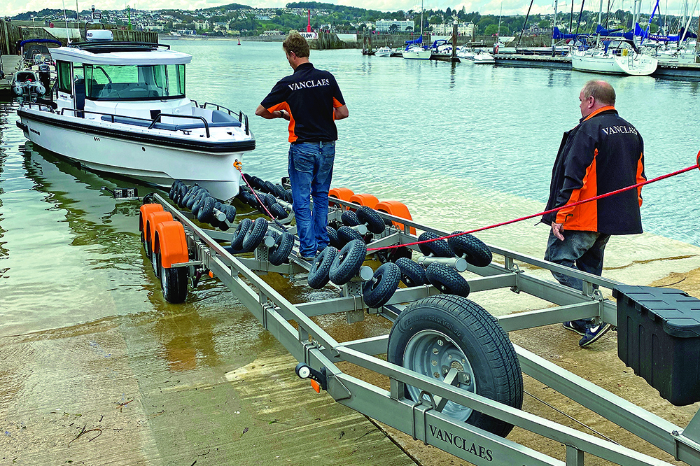 Axopar 28 Cabin on Vanclaes triple-axle trailer ready for towing, hitched to Land Rover Defender at marina slipway