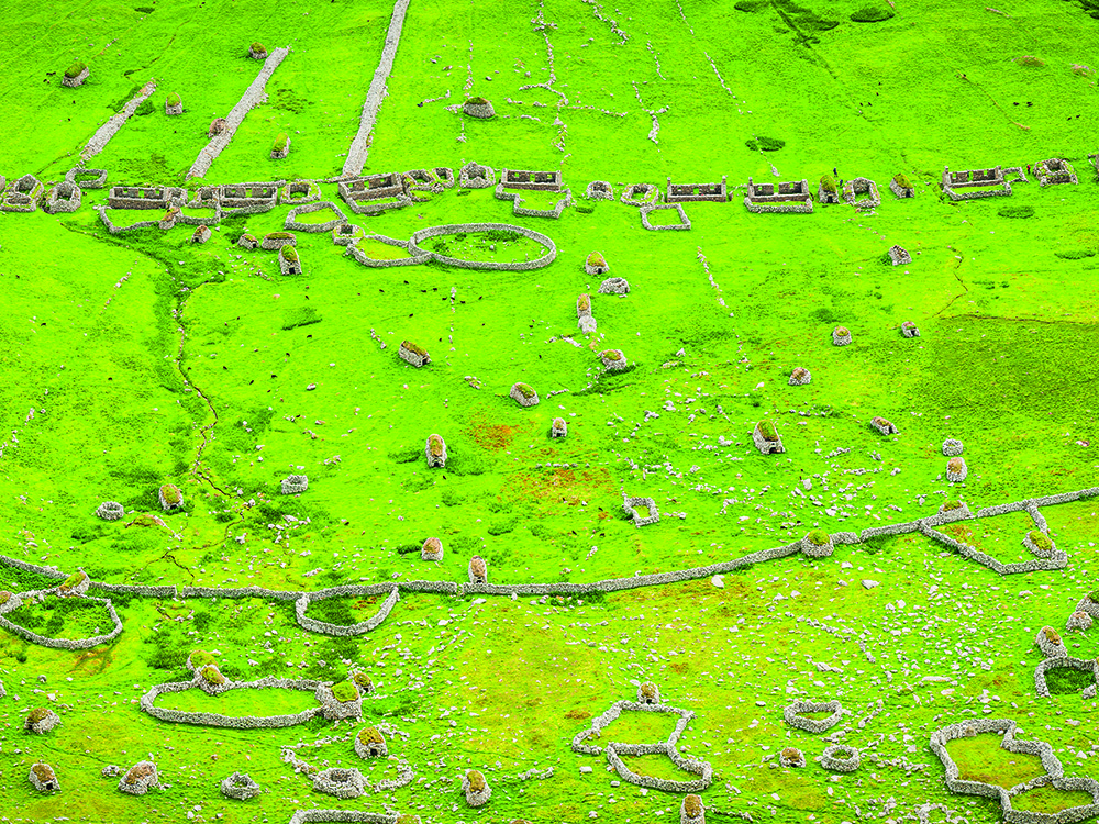 Stone cleits and ruined field walls scattered across vivid green grass on St Kilda, showing the remains of the island’s historic settlement.
