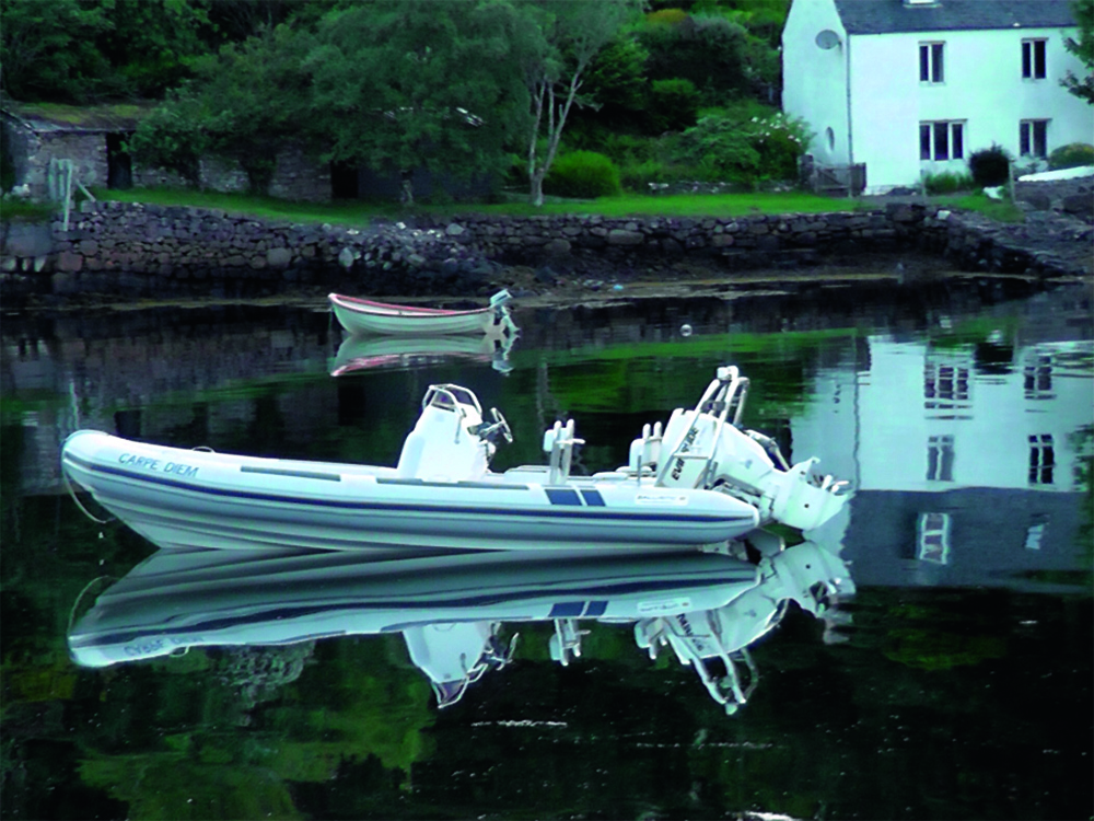 White RIB named Carpe Diem moored on calm reflective water at Badachro, with houses and stone walls along the shoreline.