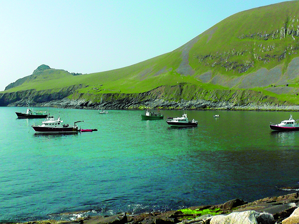 Boats anchored in the turquoise waters of Village Bay, framed by steep green cliffs on Hirta in the remote St Kilda archipelago.