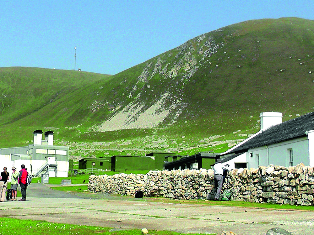 Visitors walking through Village Bay on St Kilda, with restored cottages, the NTS buildings and steep green hills behind.