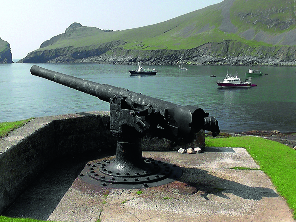 A rusted First World War gun overlooking Village Bay on St Kilda, with visiting boats anchored below the steep green cliffs.