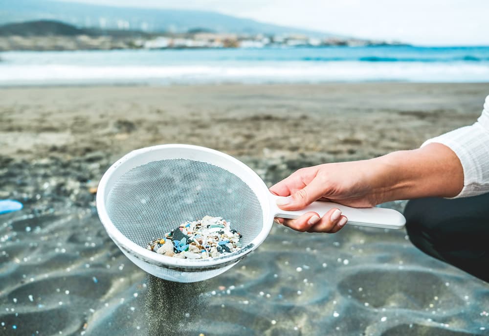 Young woman cleaning microplastics from sand on the beach - Environmental problem, pollution and ecolosystem warning concept