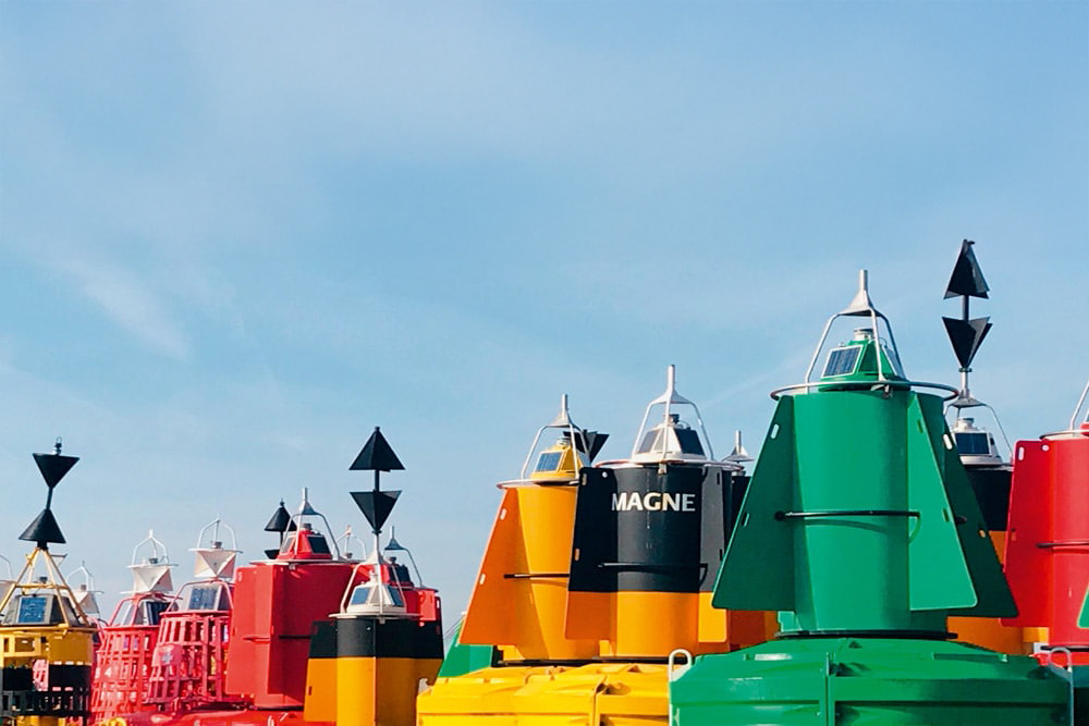 Red, green and yellow navigation buoys including lateral and cardinal marks stored ashore in harbour yard.