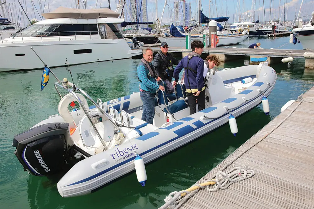 Crew practising marina berthing on a RIB with outboard engine, fenders deployed alongside pontoon docks