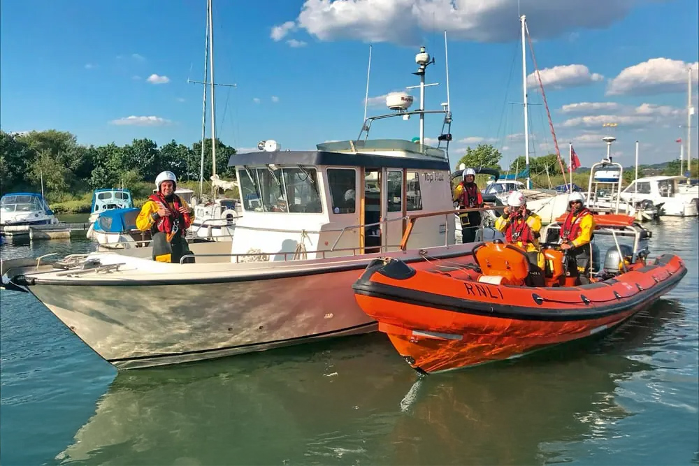 RNLI crew in orange RIB alongside cabin cruiser in marina during safety or training exercise