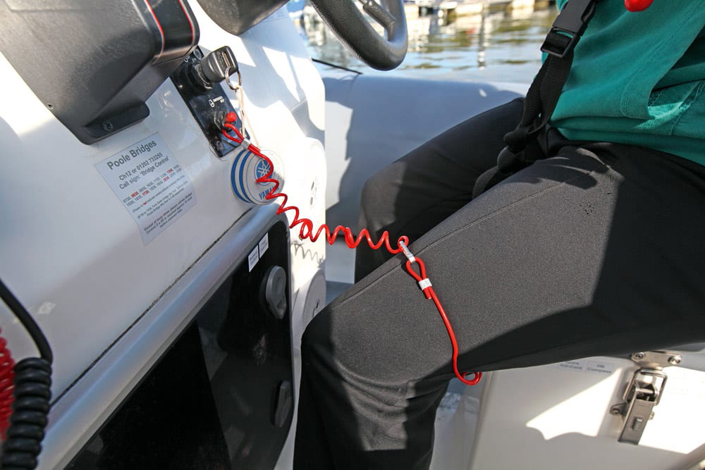 Red kill cord attached to skipper’s leg at helm, demonstrating safe powerboat operation in marina