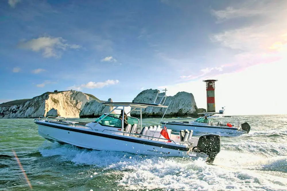Two powerboats running offshore past chalk cliffs and a lighthouse.