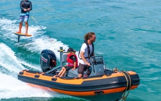 Orange Highfield RIB with man and child on board and another man wakeboarding off the stern