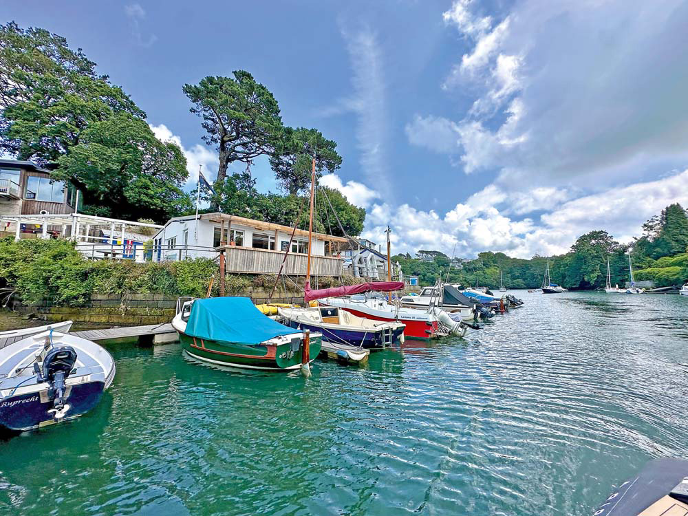 Small boats moored outside the rustic Port Navas Yacht Club, under bright summer skies.