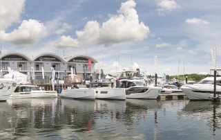 View of boats moored up at marina with boathouse in background.