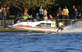 Ben Jelf’s Formula 1 powerboat skims across Oulton Broad at speed, with spectators watching from the riverbank during a record lap.