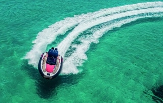 High-performance PIRELLI 35 speedboat making a sharp turn on clear turquoise water, leaving a wide wake trail behind.