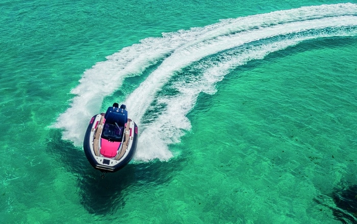 High-performance PIRELLI 35 speedboat making a sharp turn on clear turquoise water, leaving a wide wake trail behind.