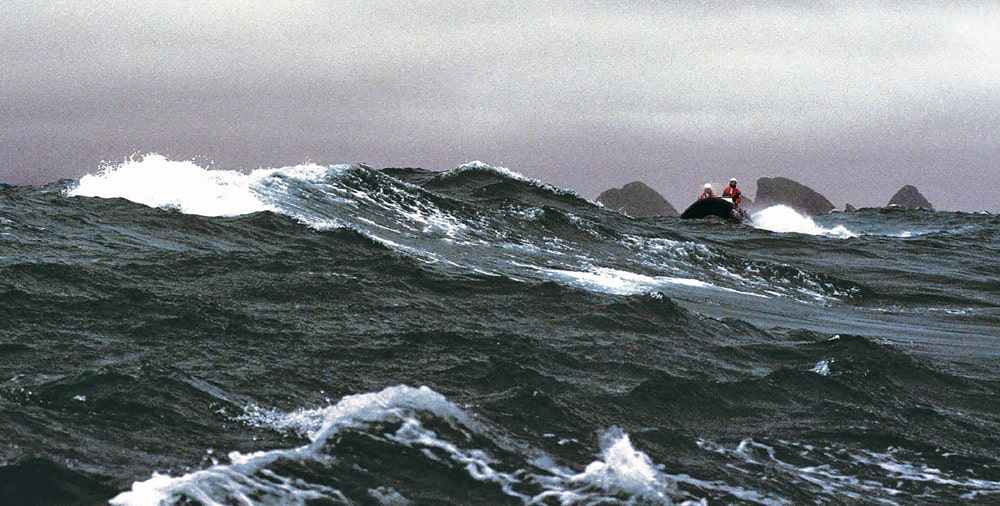 With the Stag Rocks in the background, a big sea sweeps across the path of one of the RIBs as it crests a wave.
