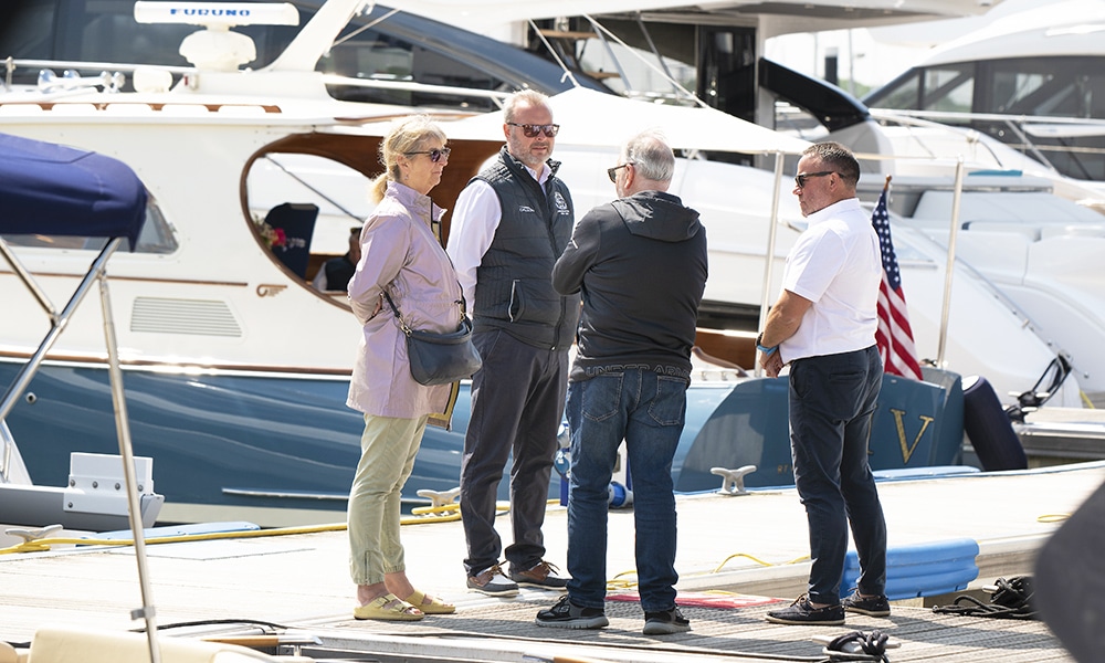 A couple standing on the pontoon talking to sales representatives at a boat show with motoryachts in the background