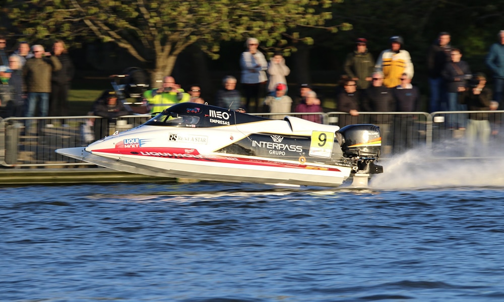 Ben Jelf’s Formula 1 powerboat skims across Oulton Broad at speed, with spectators watching from the riverbank during a record lap.