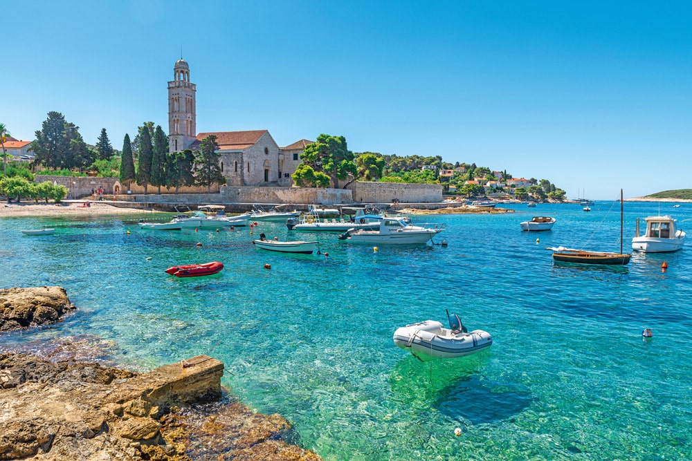 Turquoise water of Adriatic sea bay on Hvar island with franciscian monastery and boats in Dalmatia region, Croatia. Summer vacation destination