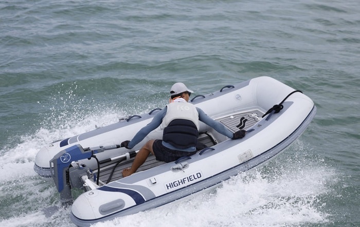 Man driving a Highfield inflatable boat at speed using a Momentum M10 electric outboard on open water.
