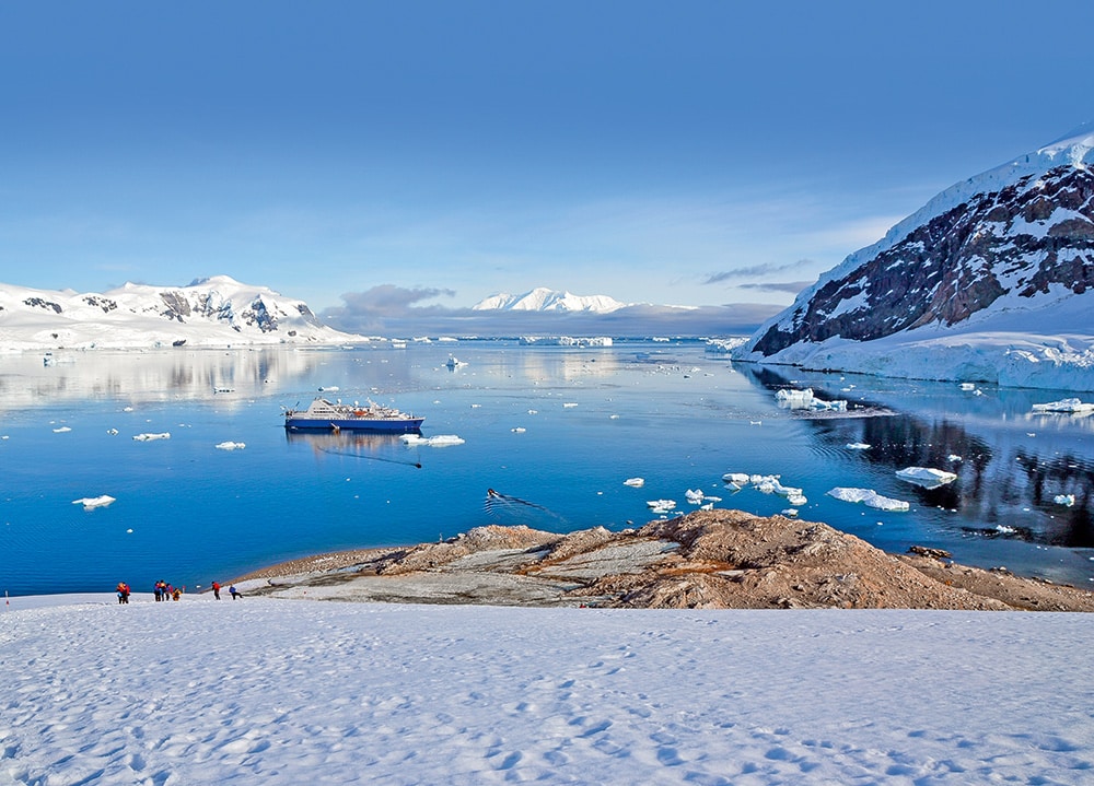 People come off the cruise ship to hike up the Antarctic hill. © iStock/namchetolukla