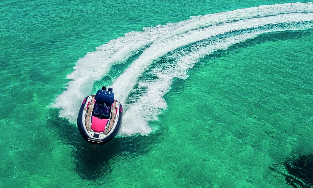 High-performance PIRELLI 35 speedboat making a sharp turn on clear turquoise water, leaving a wide wake trail behind.