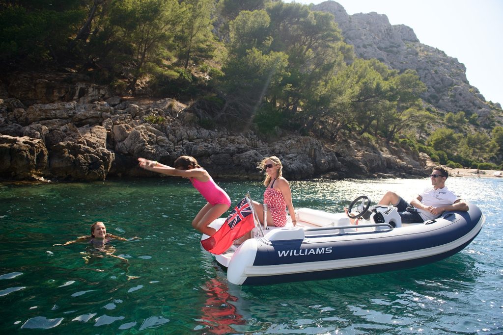 Family enjoying time at anchor in small boat with child jumping off to swim
