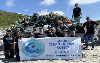 Team of Suzuki Marine volunteers standing on a beach in front of a trailer loaded with marine debris collected during a coastal clean-up.