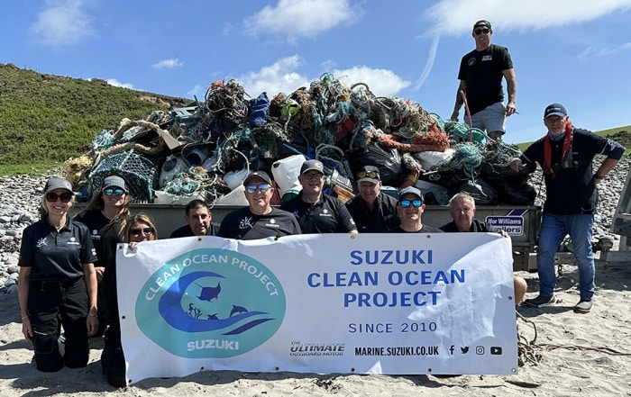 Team of Suzuki Marine volunteers standing on a beach in front of a trailer loaded with marine debris collected during a coastal clean-up.