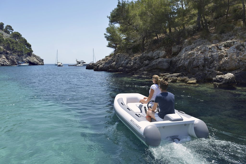 Little boat powering out of a bay towards anchored yachts