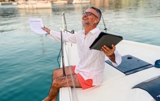 Man on boat looking up happy into sky holding tablet and paperwork