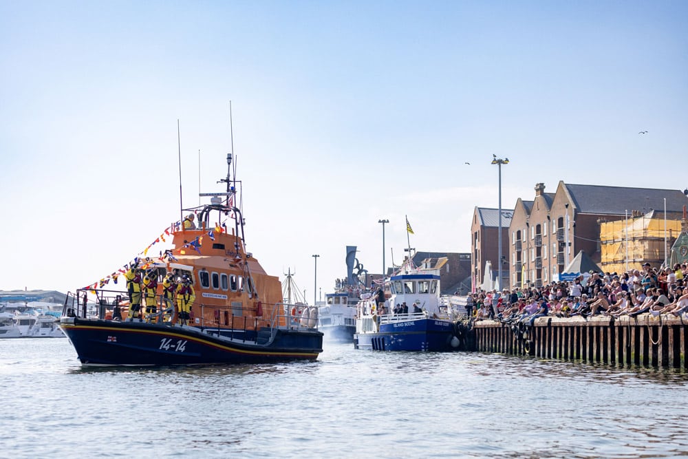 A Trent class all-weather lifeboat taking part in the flotilla as crowds gather Poole Quay. Flotilla at Poole RNLI Lifeboat Festival - 2024