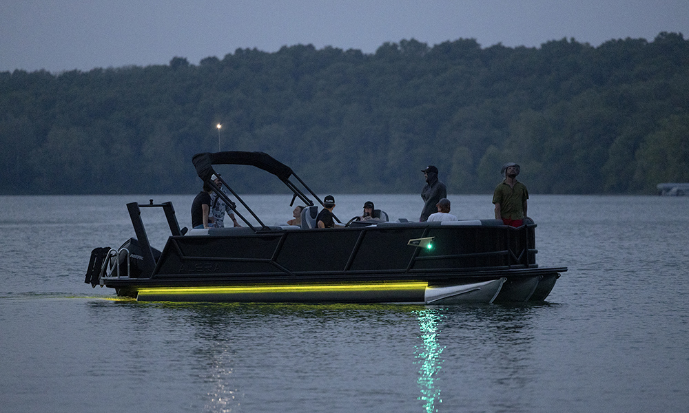 Alera Model M pontoon boat gliding at dusk with LED lighting and multiple passengers.