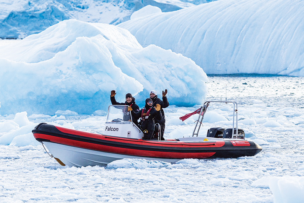 People on board red RIB in front of iceberg waving at camera