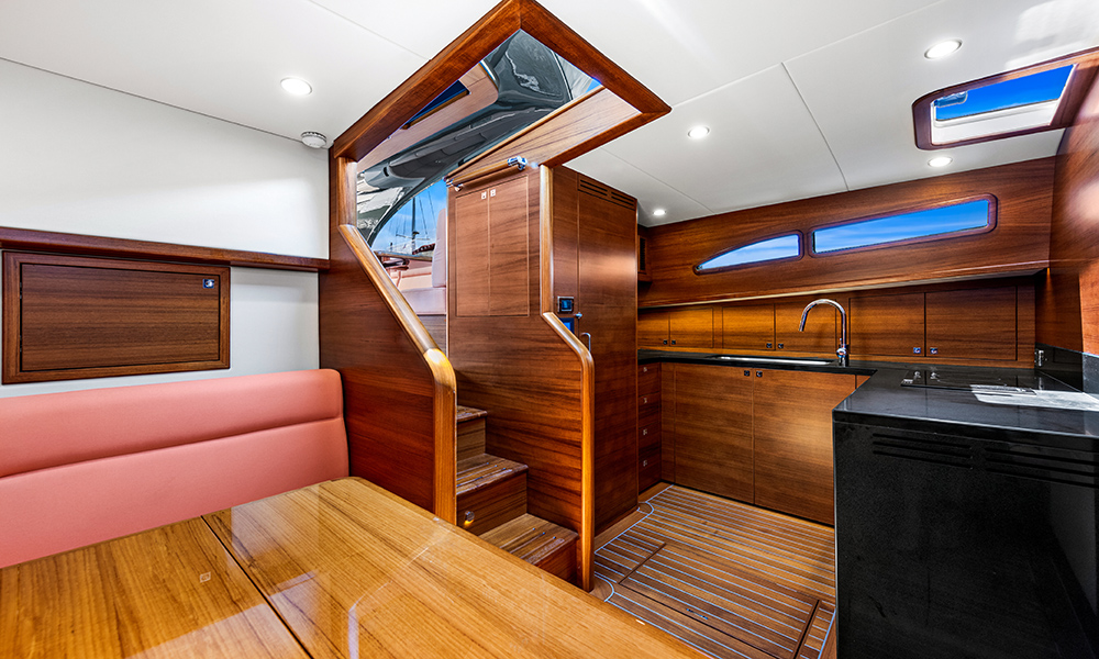 Warm teak cabinetry, a black stone galley, and pink upholstered seating showcase the custom interior of the Palm Beach GT60 Jet Drive.