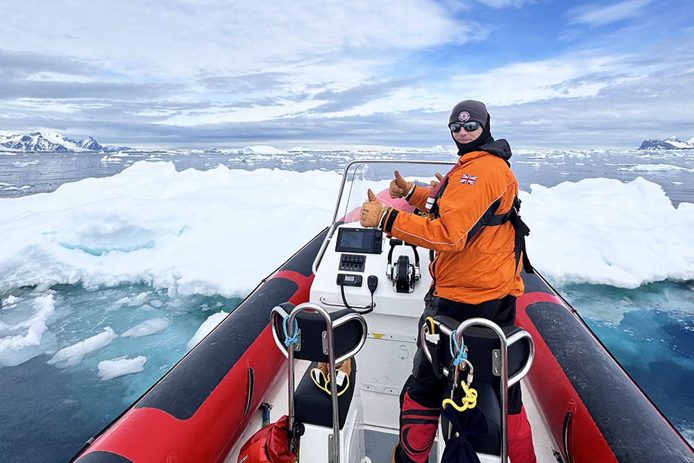 Helmsman of RIB turning back to face camera and giving two thumbs up with icebergs in background