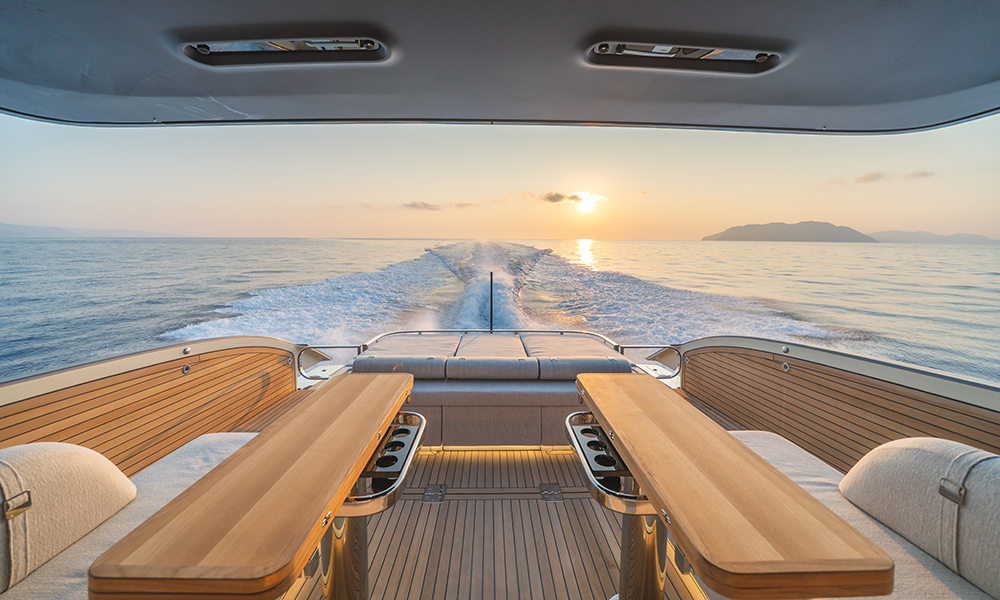 Invictus Yacht's TT550 aft deck with carbon-fibre hardtop, twin dining tables and sunpad, overlooking calm sea.
