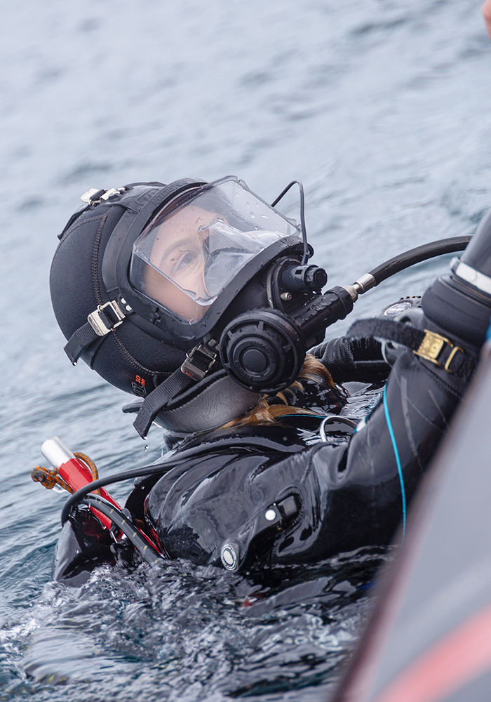 A diver surfacing and holding on to the edge of a boat.