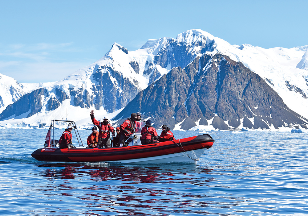 Red RIB on the water, full of people eaving with ice capped mountains behind