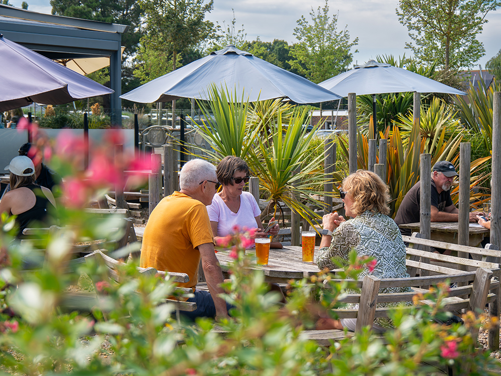 People sat at cafe tables with beers on the table and parasol