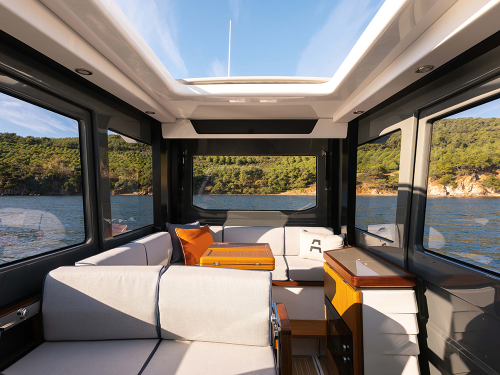Aiata Wayfinder 38 with panoramic windows, skylight, modular seating, and dining table overlooking coastal scenery.