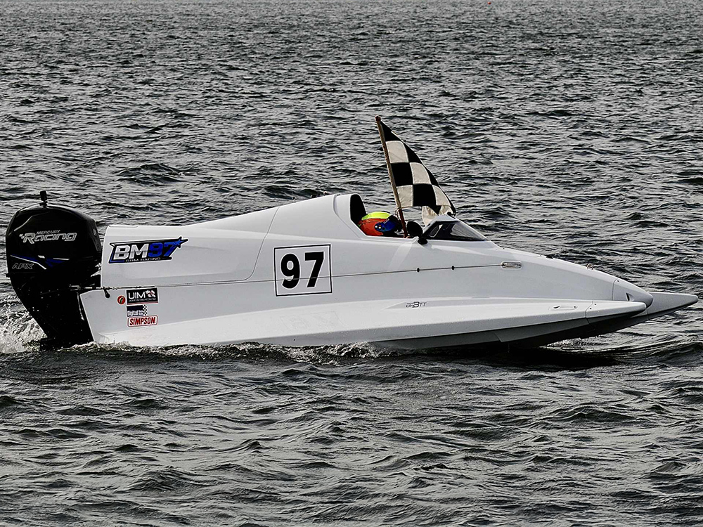 Ben Morse steers powerboat No.97 with a chequered flag raised after winning the 2025 CPA F4 British Sprint Championship.