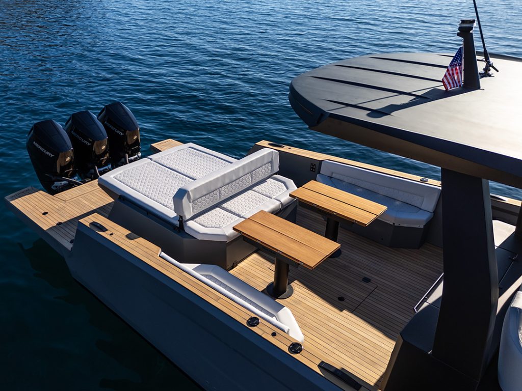 Maxim Yachts' Max 43 Comfort’s aft deck with teak flooring, twin tables, cushioned seating, sunpad and triple Mercury outboard engines.
