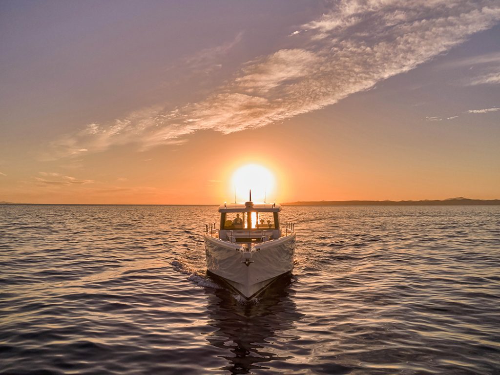 Omikron’s OT-60 yacht cruising at sunset, framed by golden light over calm open water.