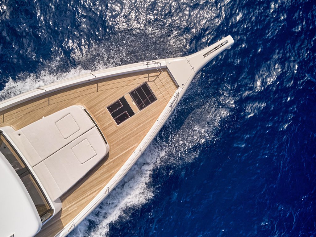 Bow view of Omikron’s OT-60 yacht cruising in blue waters, showcasing teak deck, sunpads, and sleek modern design.