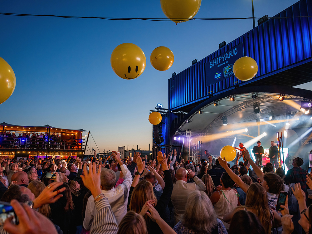Crowds enjoy live music at Southampton Boat Show’s Shipyard stage, with yellow balloons and stage lights creating a festival atmosphere.