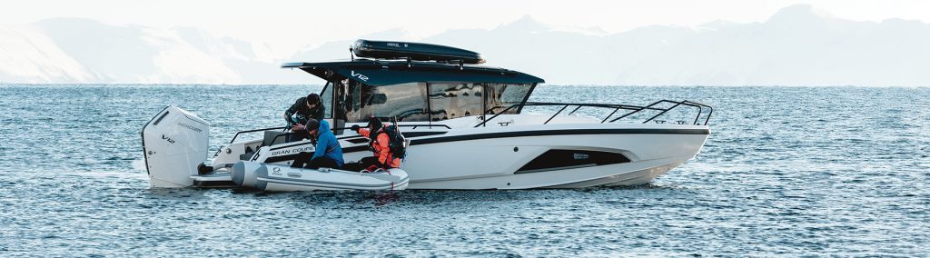 Nordkapp boat on the sea with snowy mountains behind and people in a tender in front in cold weather clothing