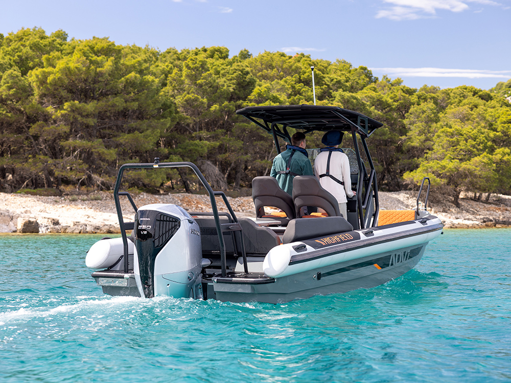 Highfield ADV7 RIB powered by Honda BF250 outboard cruising clear turquoise waters near a forested shoreline.