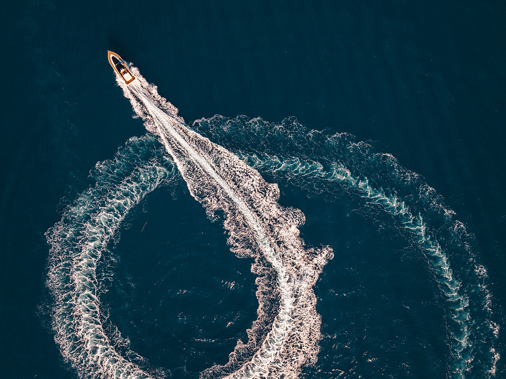 Powerboat makes a sharp turn at speed, carving a wide wake pattern across deep blue water.